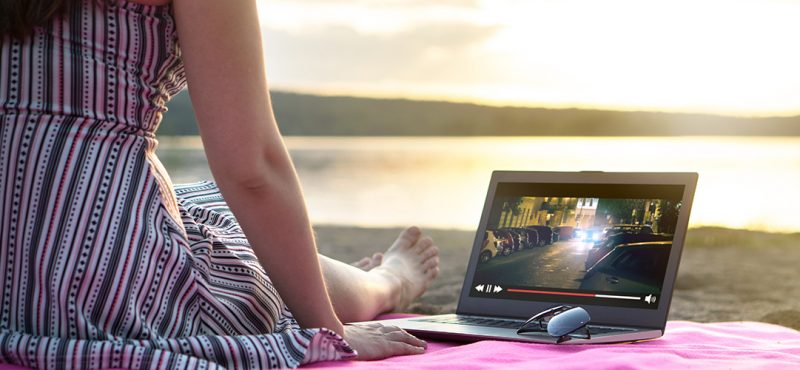 A woman sitting on a beach watching a tv show on her laptop