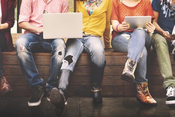 young people sitting on a bench and using laptops and tablets together