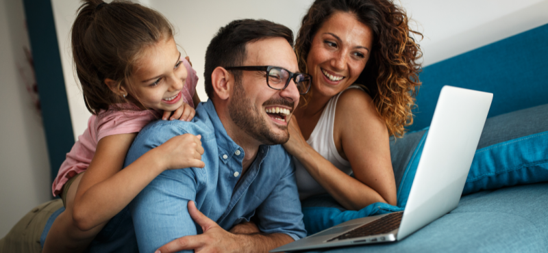 Family laughing while using a laptop.