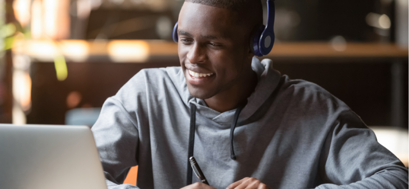 A high school student with headphones attends a virtual class on his laptop.