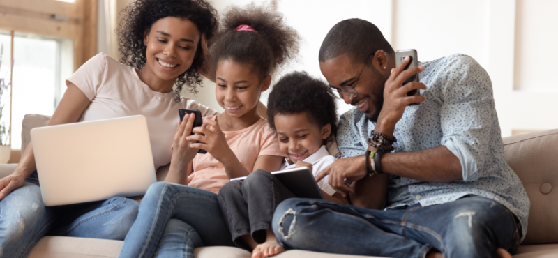 Family on a couch using multiple Wi-Fi enabled devices.