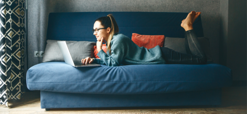 A female college student attends an online class from her couch.