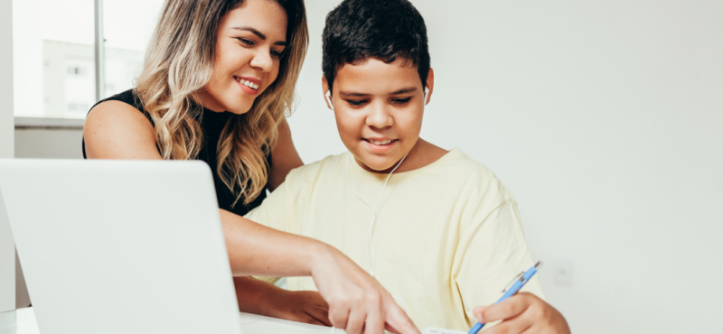 A mother helps her young son complete schoolwork on a laptop.