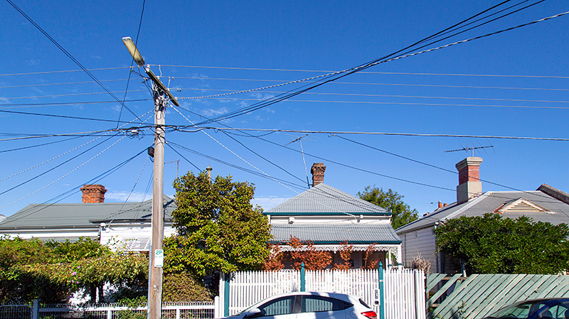 A telegraph pole has many crossing over cables running into the houses on the street.