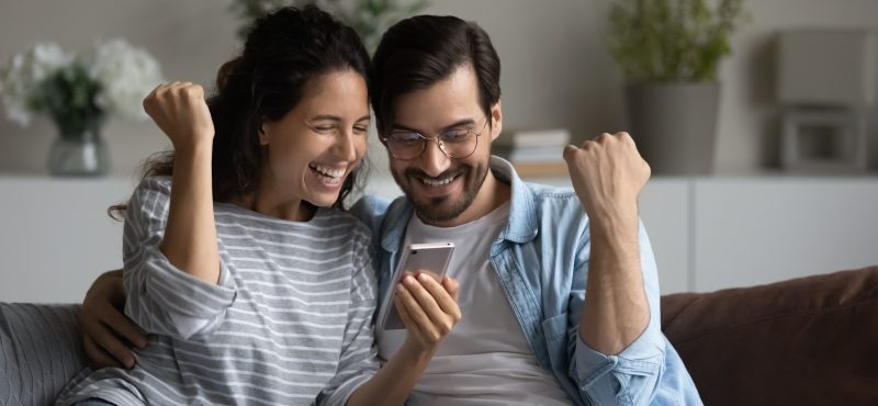 a couple celebrates together while looking at their phone
