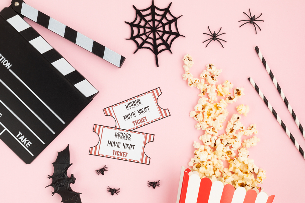 Movie clapperboard and halloween decoration over pink background.